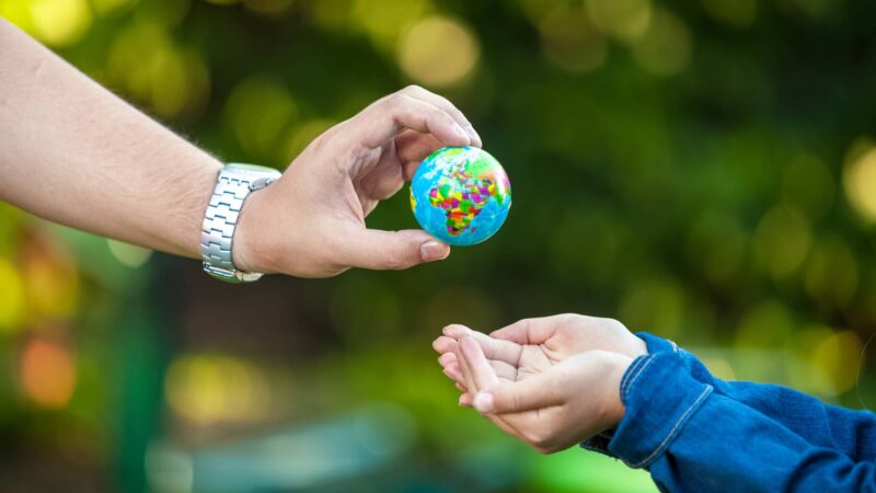 man giving Earth globe to little girl Adult man giving Earth globe to little girl