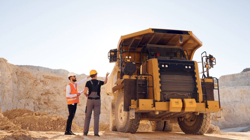Standing near haul truck and talking about document. Two men in uniform are working together in the quarry.